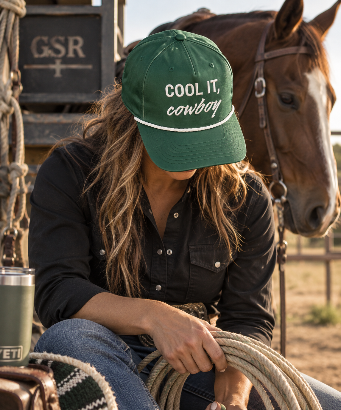 Woman wearing a green Cool It Cowboy rope cap while holding a lariat beside a horse at the ranch
